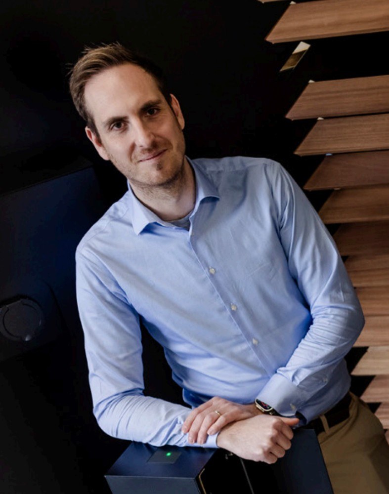 Jens Téblick, leaning on a charging unit with a green status light.